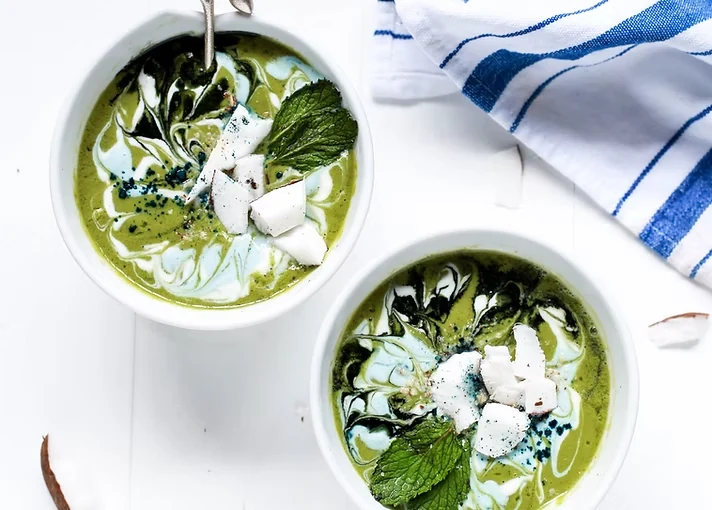 Two green smoothie bowls topped with coconut and mint