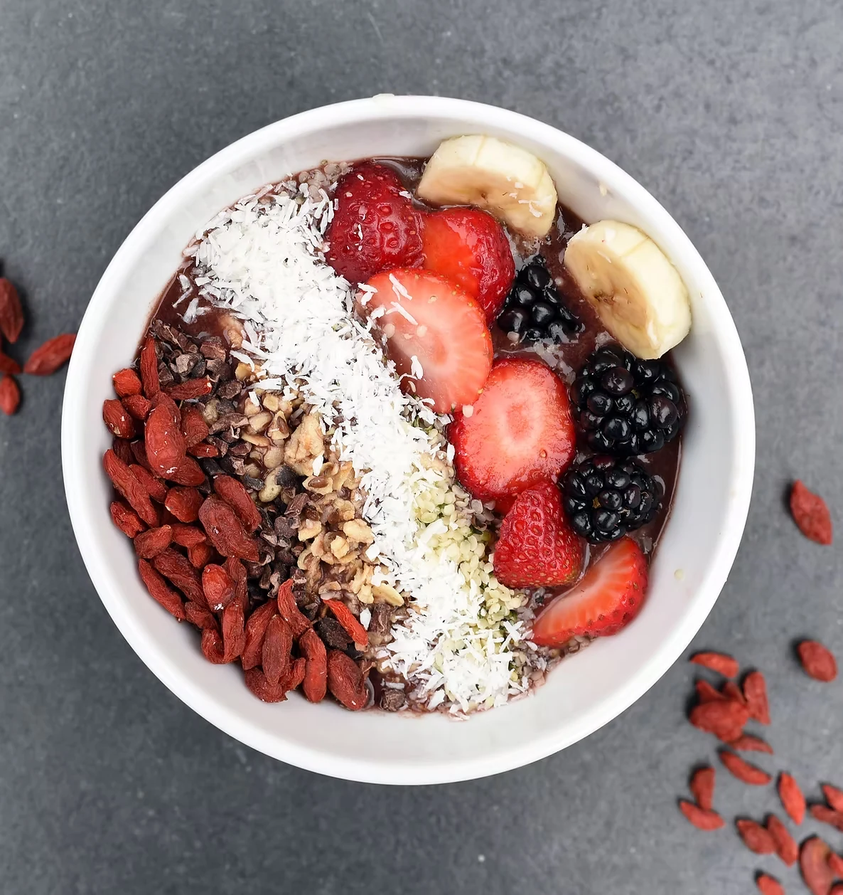 A smoothie bowl topped with berries, banana, coconut, and seeds